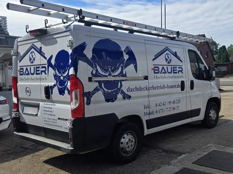 Weißer Kastenwagen eines Dachdeckerbetriebs mit blauem Logo und großem Totenkopf-Motiv