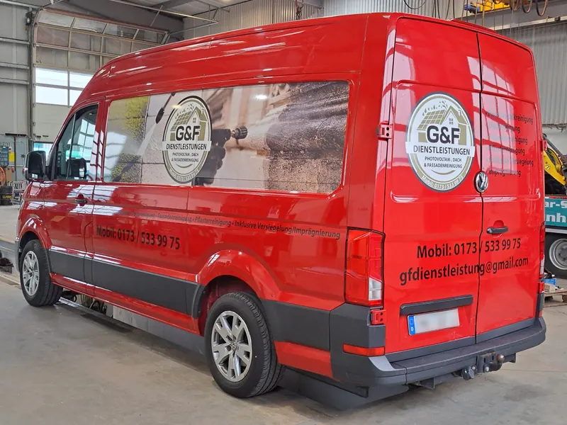 Roter Kastenwagen mit Logo, Bildmotiv in der Seitenscheibe und Leistungsübersicht am Heck