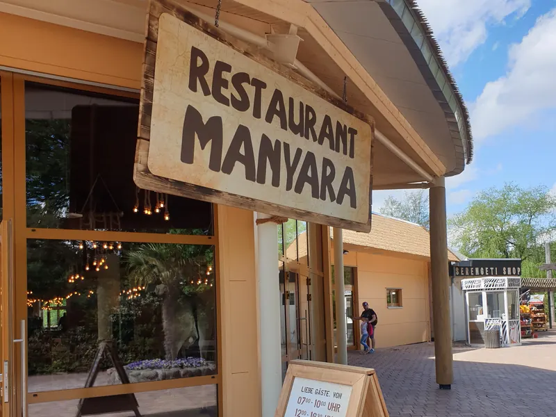 Hängeschild in Holzoptik über dem Eingang eines Restaurants, davor ein Kundenstopper