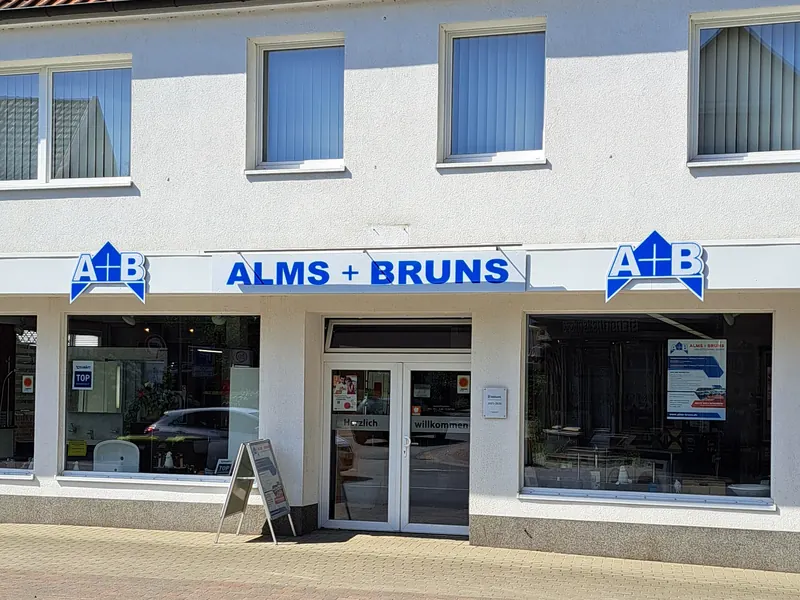 Ladenfront mit Firmenschild in Blau und zwei Logo-Formschildern über den Schaufenstern