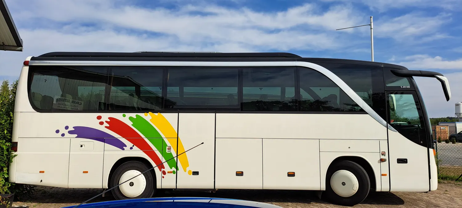 Weißer Reisebus mit altem Regenbogen-Motiv vor der Folierung